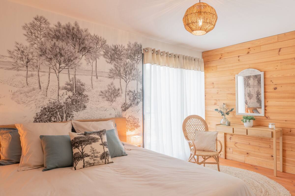 Ein Schlafzimmer mit einem großen Bett, einer Holzkommode, einem Sessel und einer Wandvertäfelung mit Baumotiv.