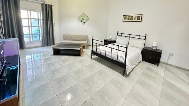A bedroom with a bed, bedside tables, a sofa, a coffee table, and a window with curtains. - Villa 126 (Dubai)