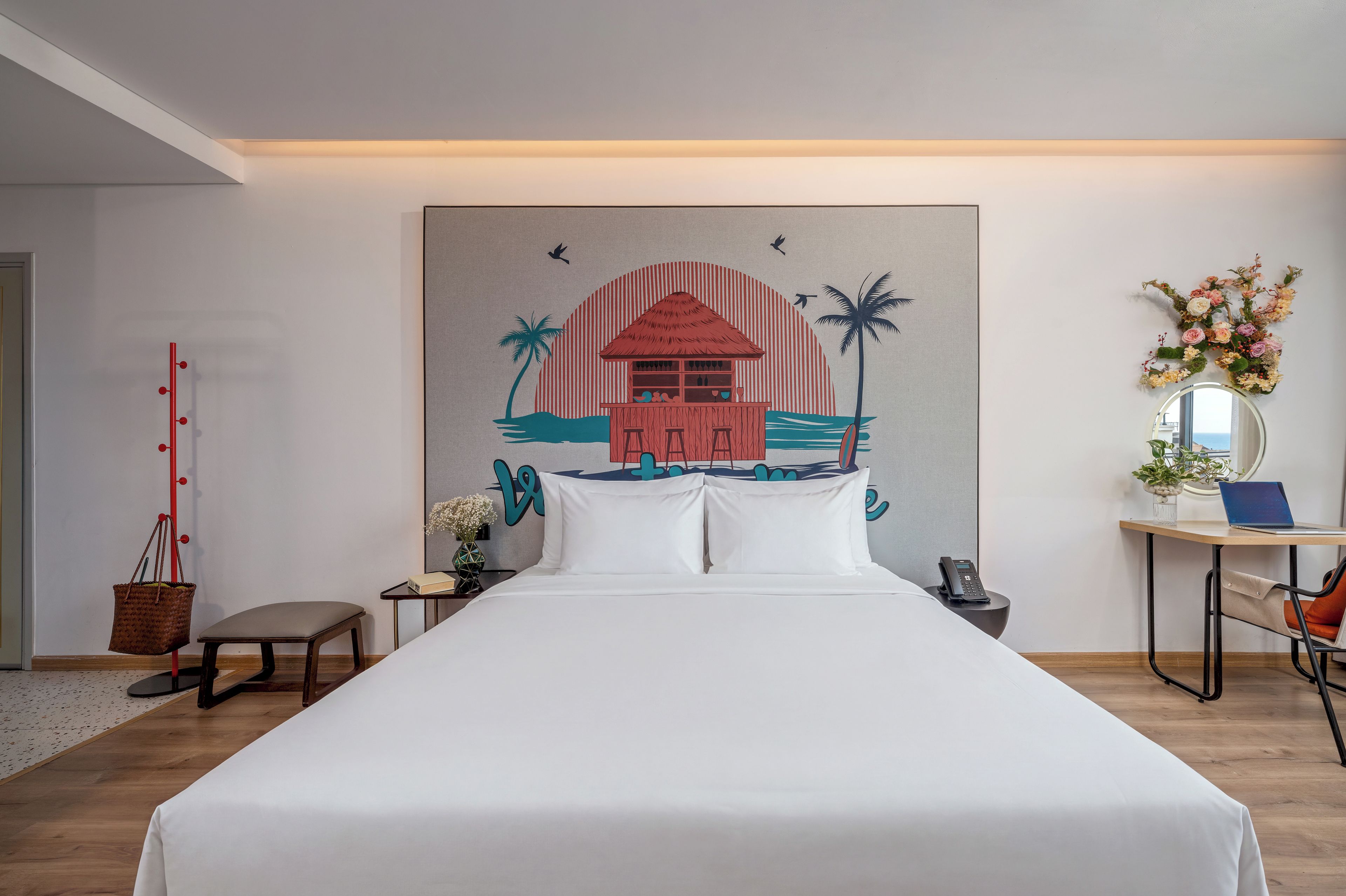 A hotel room with a large bed, a desk with a laptop, a phone, and a wall-mounted mirror.