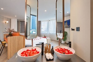 Ein Hotelzimmer mit zwei großen weißen Waschbecken, gefüllt mit Rosenblättern, einem Holztisch mit einer Vase, einem Bett mit Rosenblättern und einem großen Spiegel.