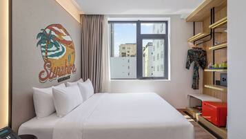 Une chambre d’hôtel équipée d’un lit, d’un téléphone, d’une fenêtre donnant sur des immeubles et d’un mur orné d’une œuvre d’art colorée.
