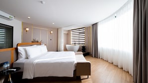 Habitación de hotel moderna con una cama grande, una mesita de noche, bañera integrada y un amplio ventanal con cortinas.
