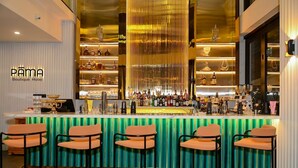 Una zona de bar con un mostrador verde a rayas y cinco taburetes naranjas.