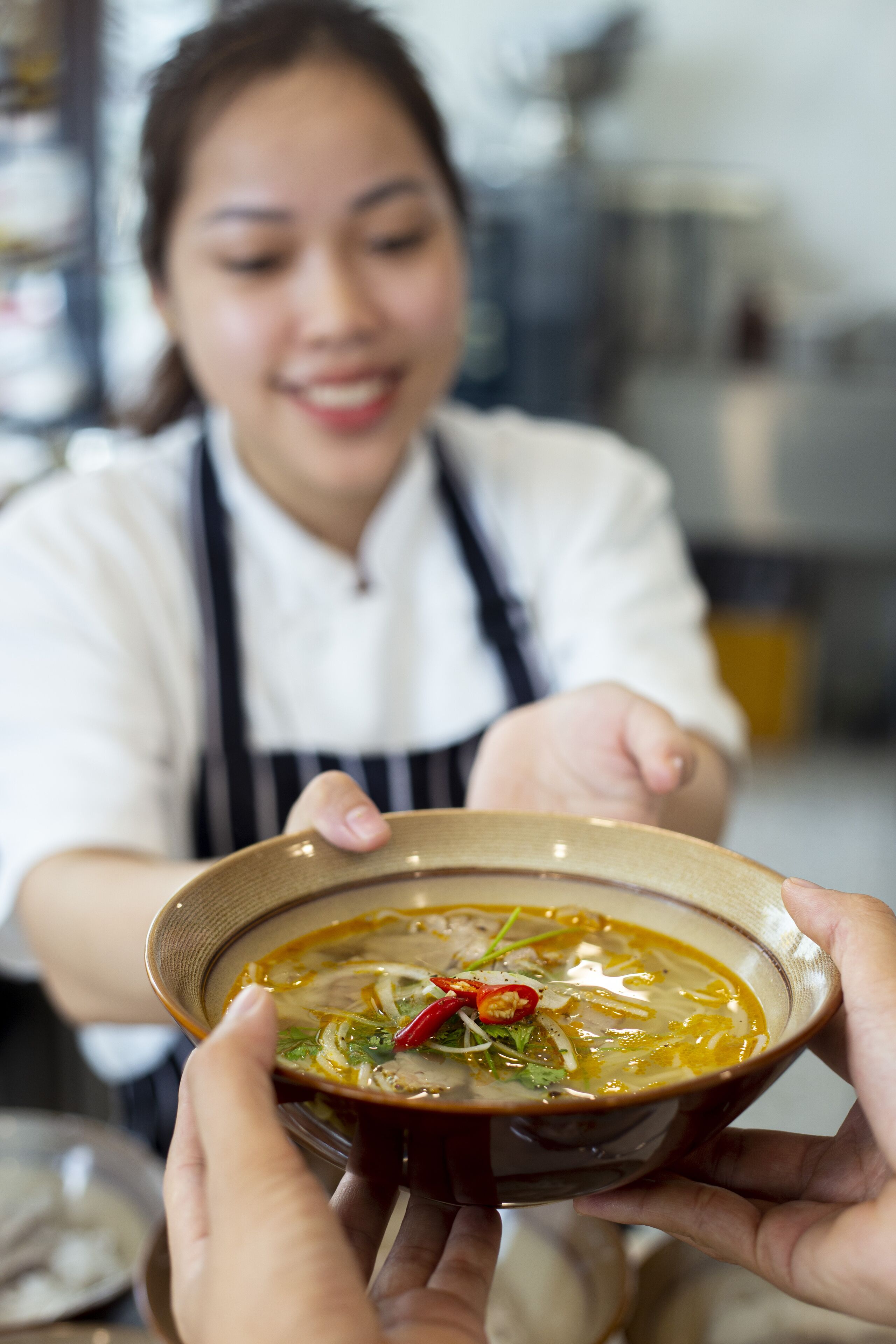 A person holding a bowl of soup, with another person reaching out to receive it.