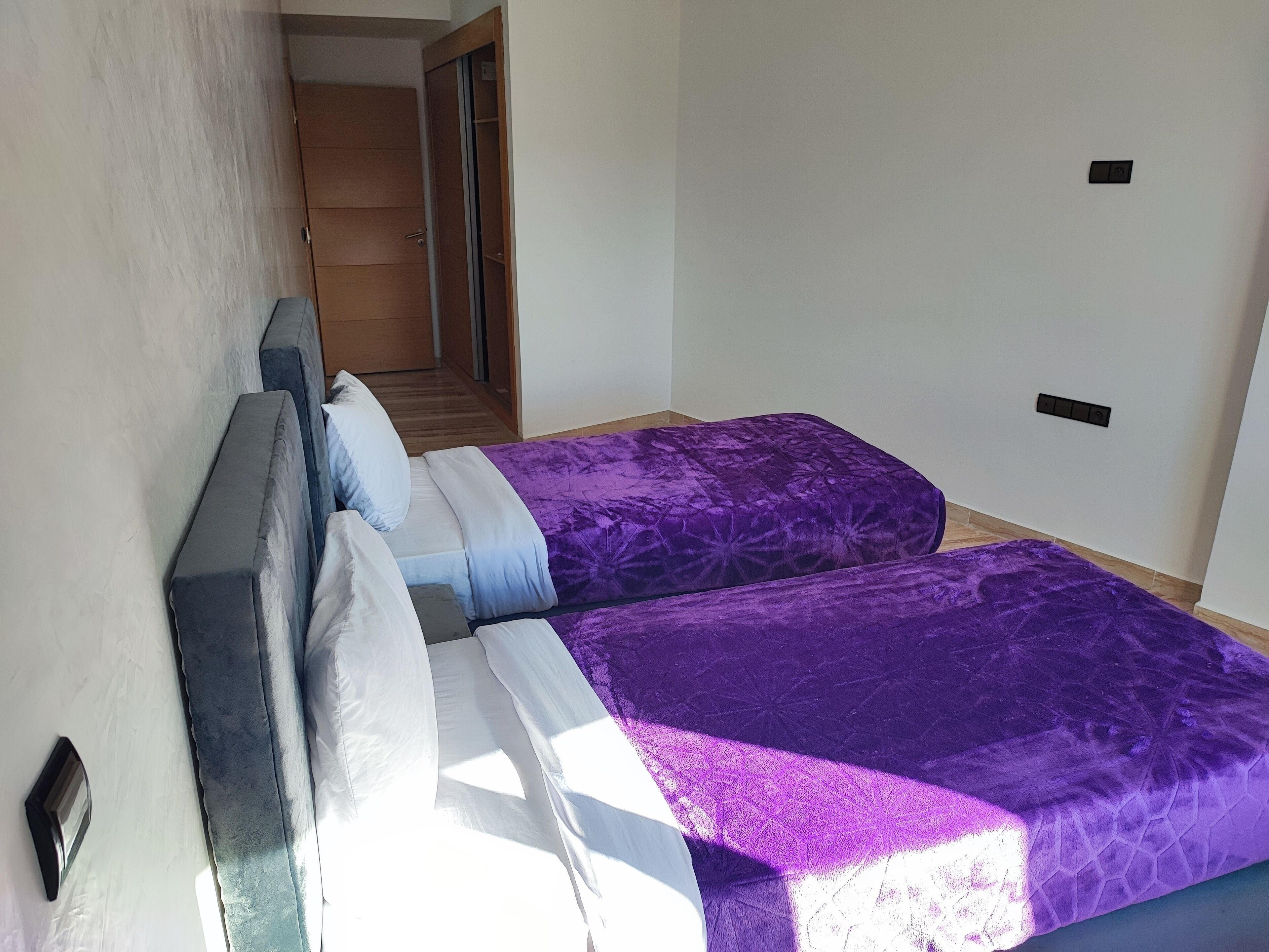 A bedroom with two beds, a wooden wardrobe, and a door leading to another room.
