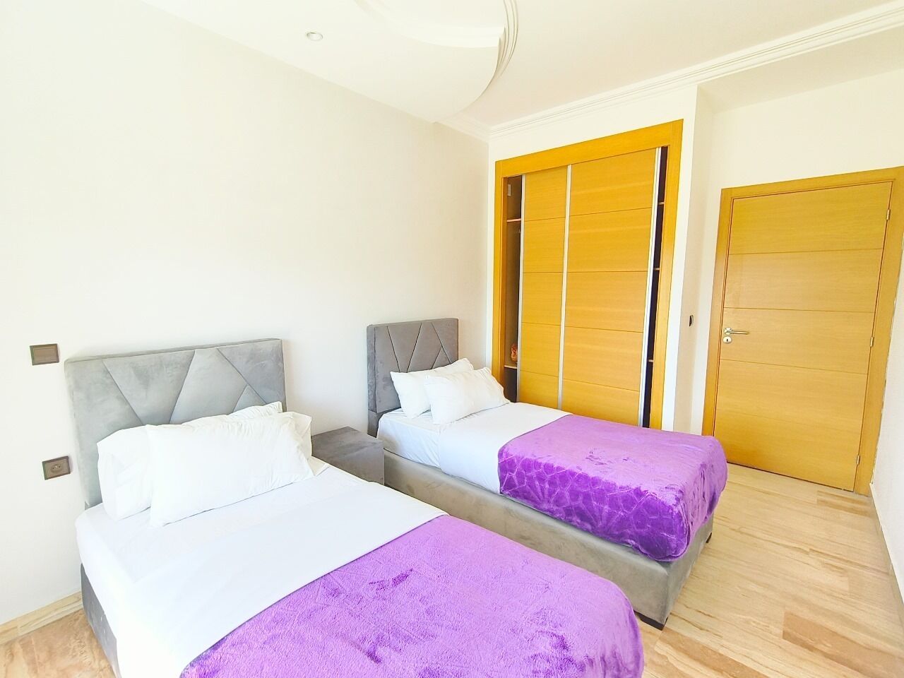 A bedroom with two beds, a wooden wardrobe, and a door.
