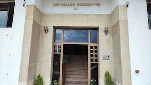 La entrada de 'LES BELLES RESIDENCES (E)' con fachada de azulejos, una escalera de madera y plantas en macetas en la base.