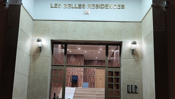 La entrada a Les Belle Residences, con un diseño moderno, que presenta una puerta de cristal, una escalera y plantas en macetas.