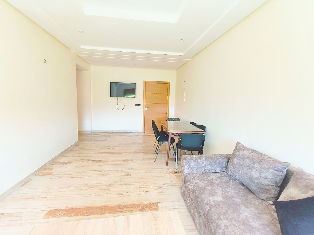 Un vaste espace de vie doté d’un plancher en bois, d’un canapé, d’une table à manger avec des chaises et d’un téléviseur fixé au mur.