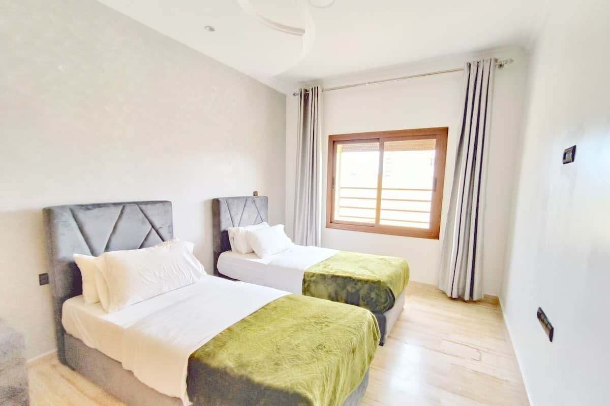 Une chambre d’hôtel avec deux lits, une grande fenêtre avec des rideaux et un plancher en bois.