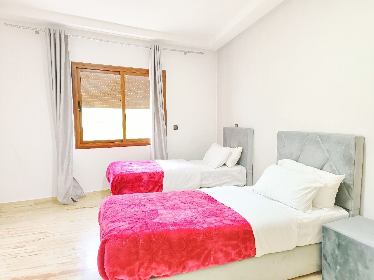 A bedroom with two beds, a window with blinds, and a wooden floor.