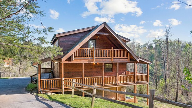 A two-story log cabin with a balcony, surrounded by a wooden fence and trees.