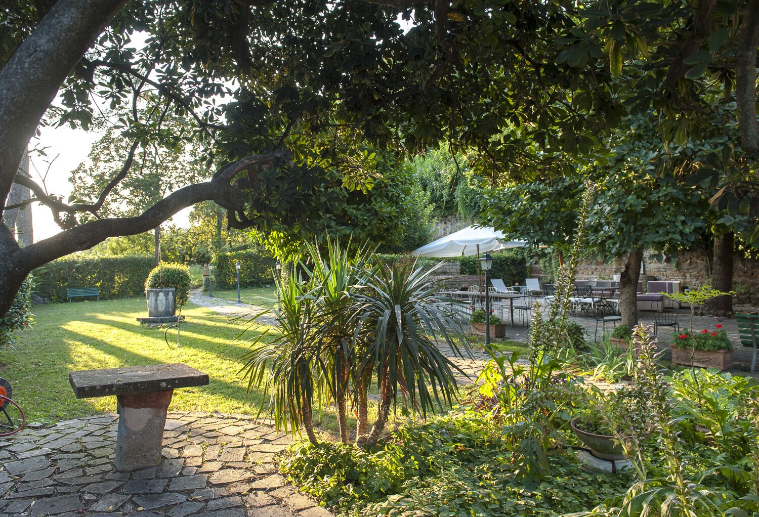 Een tuin met een stenen bankje, een tafel met stoelen en een overdekt gebied met parasols.
