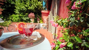 Une table avec une boisson et une serviette, entourée de verdure et adossée à un mur rose.