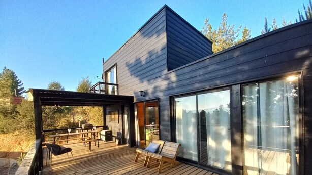 Une maison moderne dotée d’une terrasse en bois, d’un espace salon extérieur couvert et de grandes portes-fenêtres coulissantes.