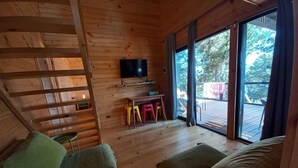 L’intérieur chaleureux de ce chalet est agrémenté de boiseries, d’un téléviseur à écran plat, d’un coin repas avec des tabourets colorés et d’une grande porte-fenêtre coulissante qui donne sur une terrasse extérieure.