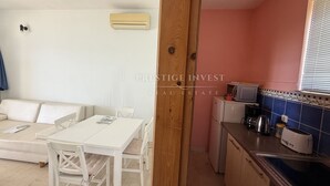 A compact living space with a white sofa, a dining table with chairs, a kitchenette with a microwave and toaster, and a wooden door. - Seafront Ground Floor (Zadar)