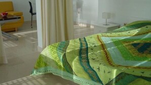 A hotel room with a bed covered in a patterned bedspread, a yellow armchair, a small table with a lamp, and a window with curtains. - Seafront Ground Floor (Zadar)
