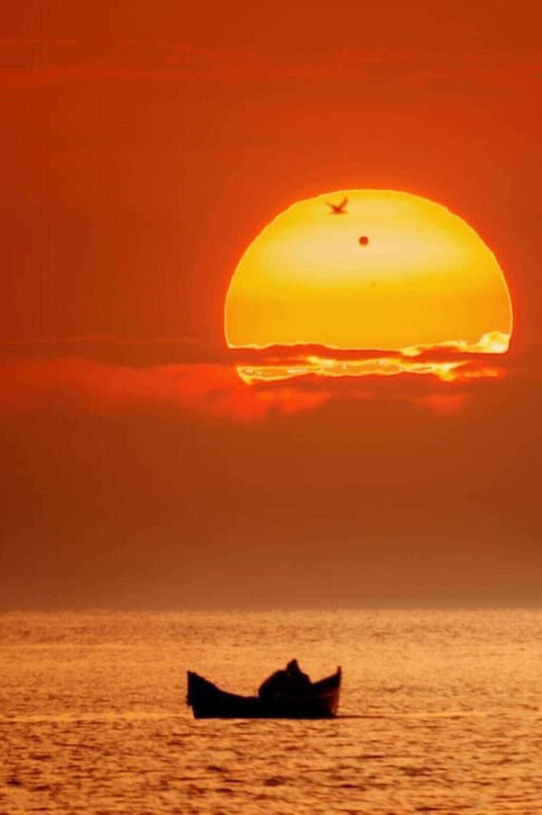 Pôr do sol sobre águas calmas, com a silhueta de um barco.