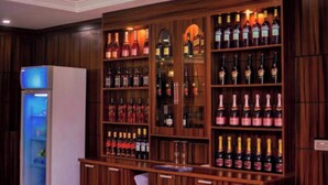 A bar area with wooden shelves stocked with various bottles, a refrigerator, and a bar counter. - Ughelli Wetland Hotel (Ughelli)