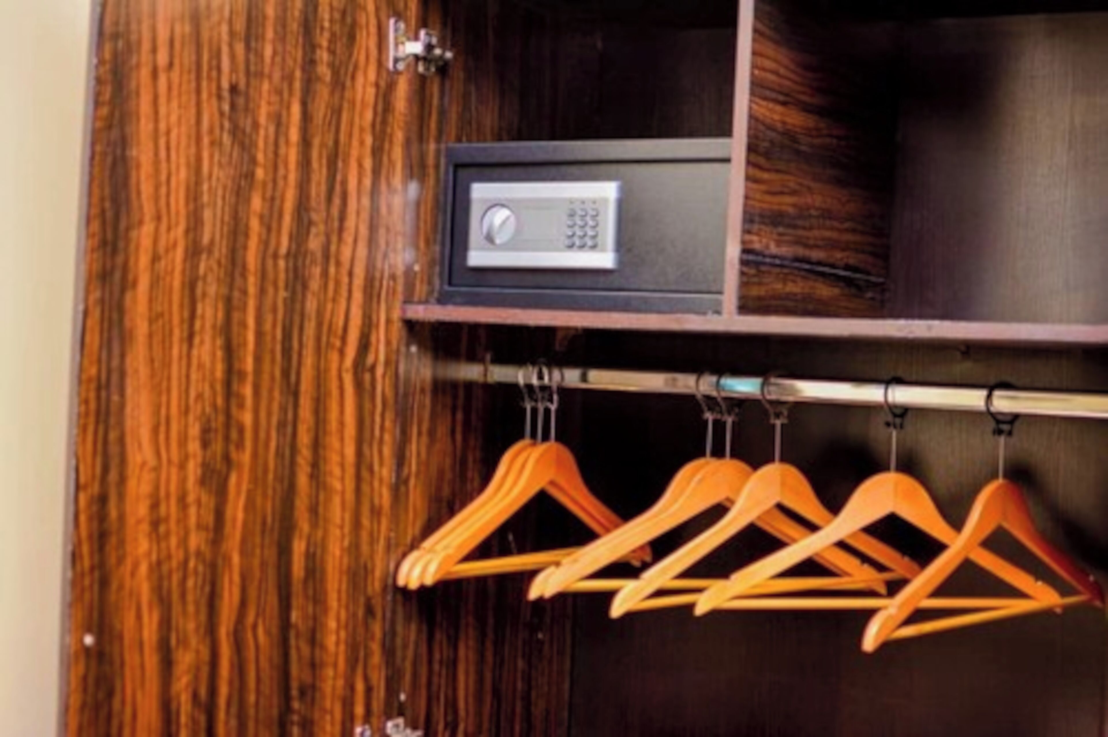 A wooden wardrobe with a built-in safe and a metal hanger rack.
