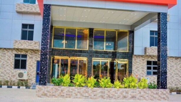 A modern building with a glass entrance, stone facade, and a red roof. - Ughelli Wetland Hotel (Ughelli)