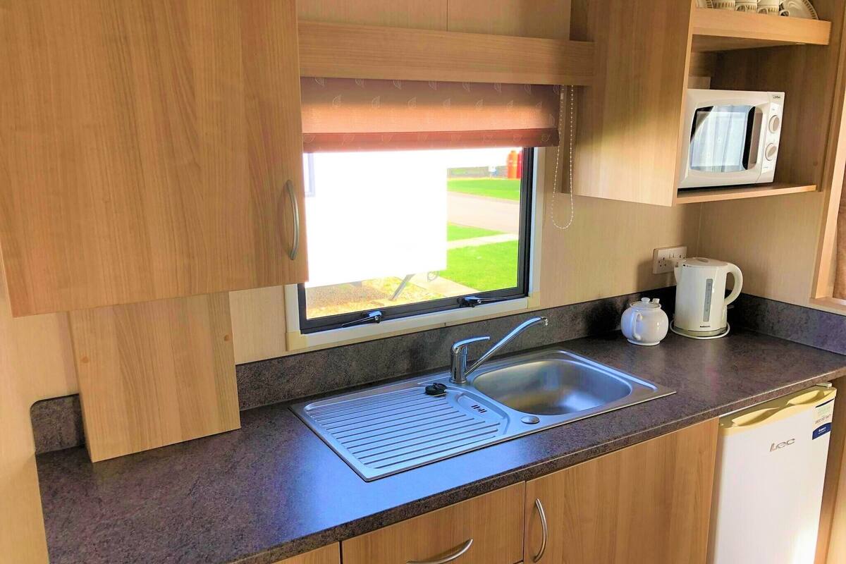 A compact kitchenette with a window, a microwave, a kettle, and a sink.
