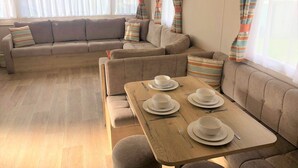 A cozy living area with a sofa set, a dining table with white plates and cutlery, and striped curtains.