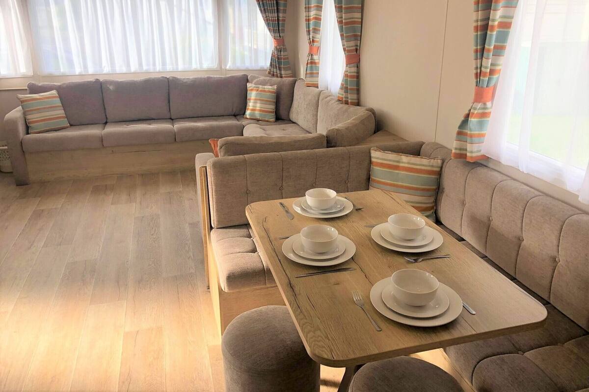 A cozy living area with a sofa set, a dining table with white plates and cutlery, and striped curtains.