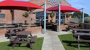 An outdoor seating area with picnic tables and red umbrellas at Woody's Bar & Restaurant.