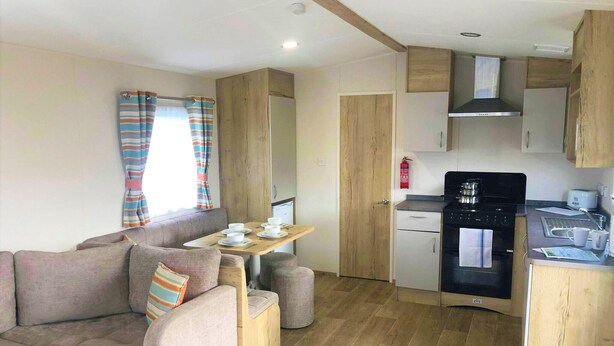 A compact living space with a sofa, a small dining table, a kitchenette, and a window with curtains.
