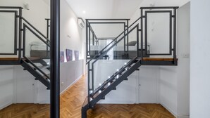 Ein modernes Interieur mit Holzdielen im Fischgrätmuster, Glasgeländern an einer Treppe und weißen Wänden.