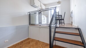 Eine moderne Küche mit weißen Schränken, einem Holzboden im Fischgrätmuster und einer schwarzen Treppe.