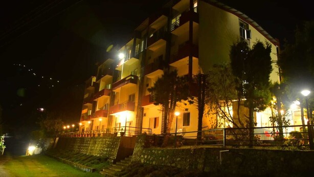 A multi-story hotel with balconies, a well-lit exterior, and a stone retaining wall.