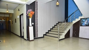 A modern hotel lobby with a staircase, a reception desk, and a decorative vase of flowers.