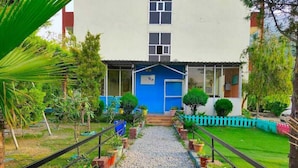 A pathway leading to a building with a blue door, surrounded by potted plants and a small fence.