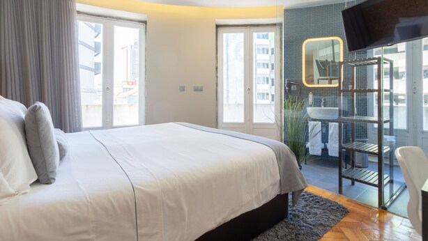 A modern hotel room with a large bed, a bathroom with a glass shower enclosure, and a view of the city. - Feel Porto Sublime Townhouse (Oporto)