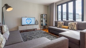 A modern living room with a grey sofa set, a flat-screen TV, a glass cabinet, and a large window with curtains. - Feel Porto Sublime Townhouse (Oporto)