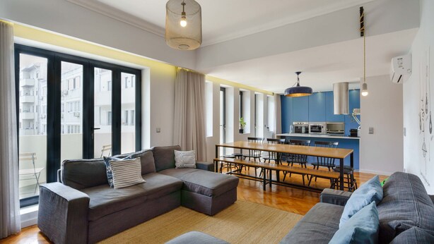 Een moderne woonkamer met een hoekbank, een eettafel en een keukenhoek.