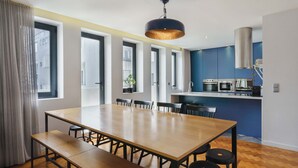 Een moderne keuken met een centraal eiland, grote ramen en een eethoek met een houten tafel en bankjes.