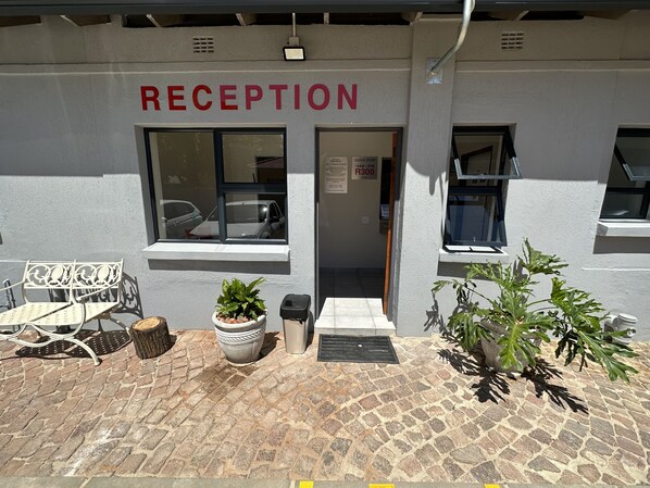A reception area with a sign reading "RECEPTION" above the door, a bench, potted plants, and a window with a view of parked cars.