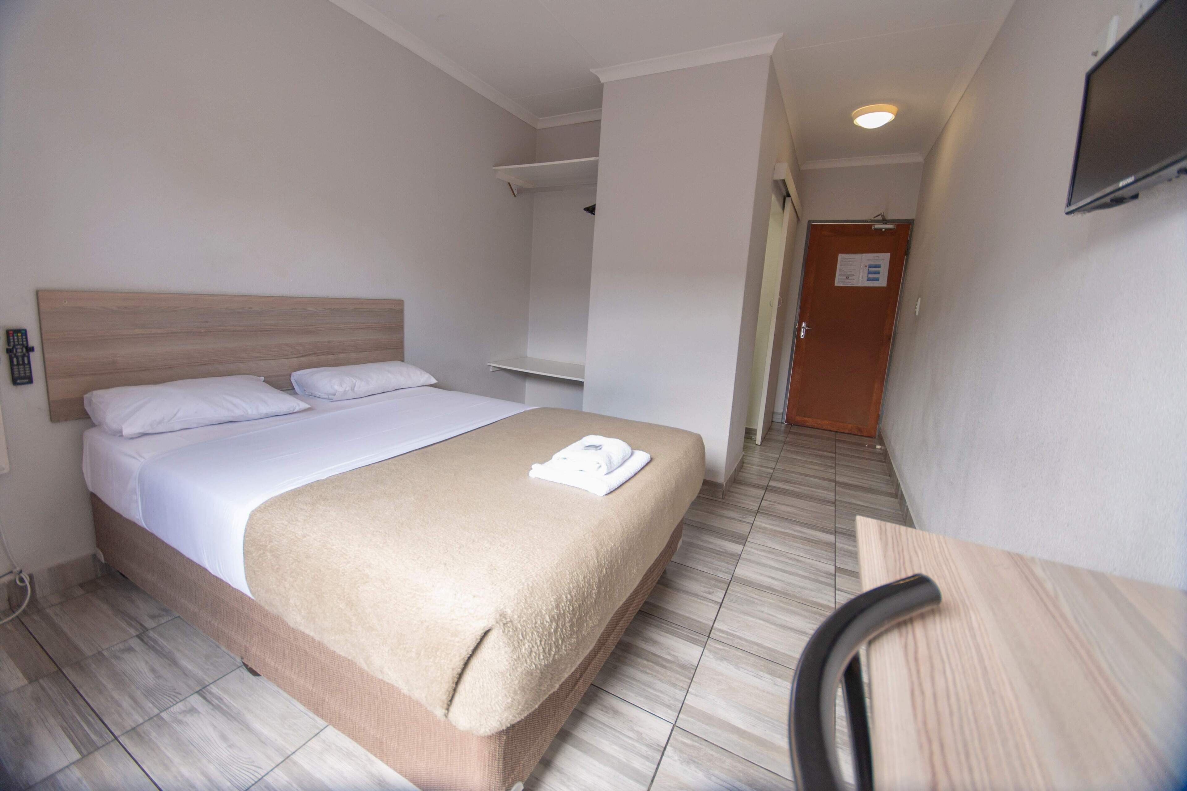 Una habitación de hotel con una cama, una silla, un televisor y una puerta.