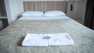 A neatly made bed with a folded towel and a remote control on the bedspread.