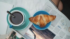 A table with a cup of coffee, a croissant, and a magazine. - My Luxury (Naples)
