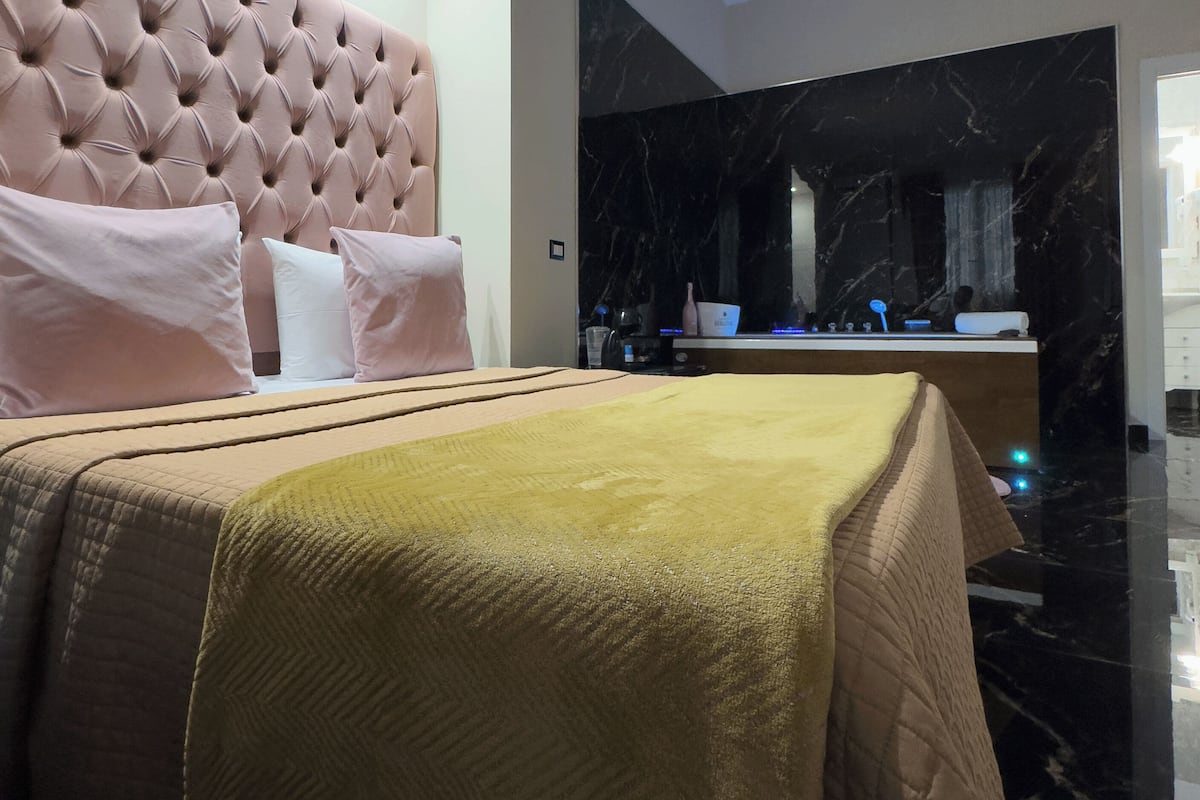 Un dormitorio moderno con un cabecero capitonado, una cama grande con colcha acolchada y una pared de mármol al fondo.