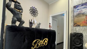 A black velvet reception desk with 'BB' monogrammed in gold, a security camera on the wall, a decorative flower wall piece, and a painting of a landscape. - My Luxury (Naples)