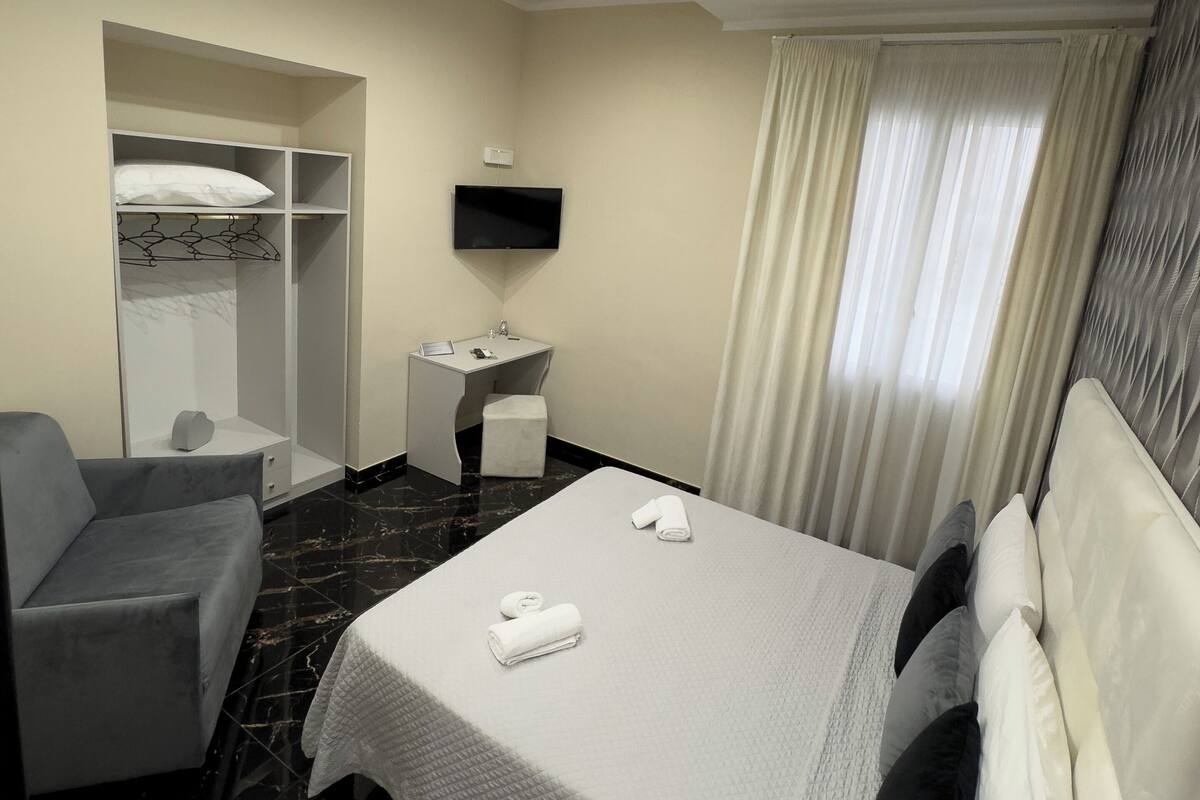 Habitación de hotel con cama, escritorio, silla, televisor y armario.