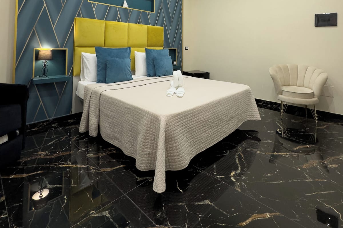 Una habitación de hotel moderna con una cama grande, un cabecero con diseños geométricos, una mesita de noche, una silla y piso de mármol.