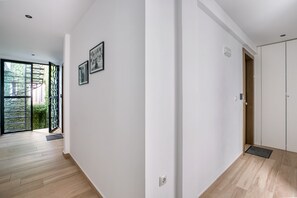 A hallway with a wooden floor, white walls, and a door leading to a room. There are two framed pictures on the wall. - Elia Kolonaki Luxury Apartments  (Athens)