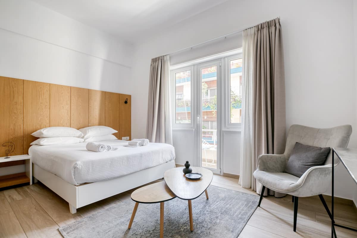 Une chambre d’hôtel moderne, équipée d’un lit, d’une petite table, d’une chaise et offrant une vue sur le balcon extérieur.